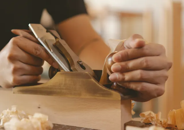 Mains d’un menuisier dressant une planche au rabot