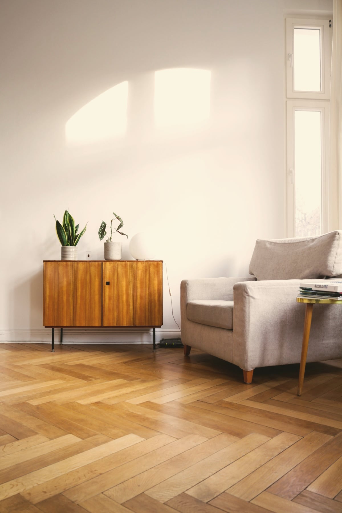 Intérieur éditorial : buffet vintage en bois, fauteuil clair et parquet en chevrons