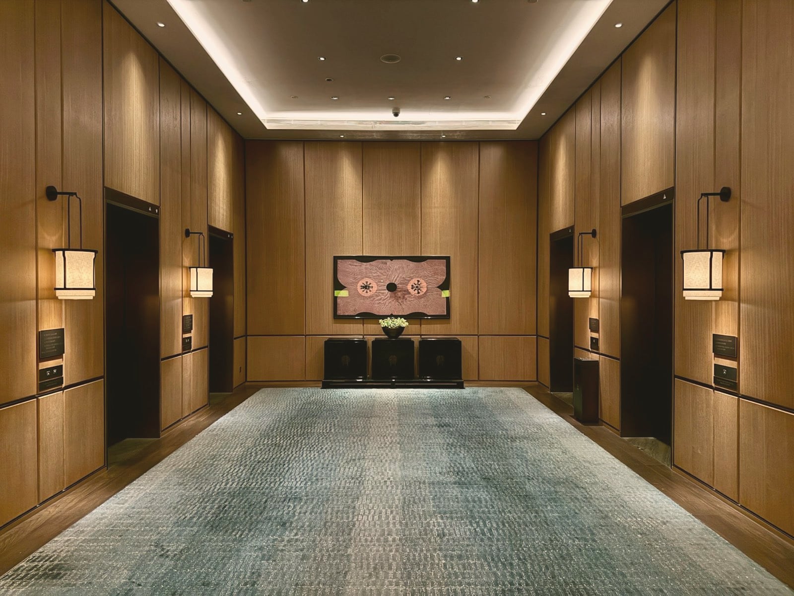 Hall d’hôtel aux boiseries claires, appliques lanternes et tapis texturé