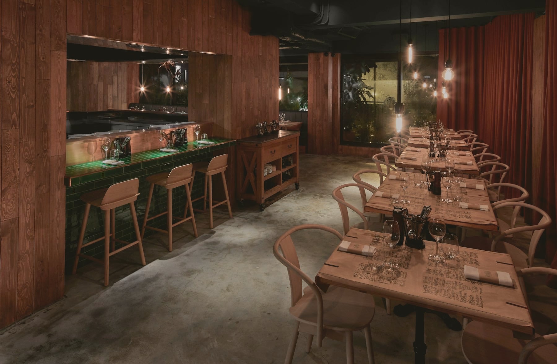 Salle de restaurant en bois sombre, longues tables dressées et chaises en bois